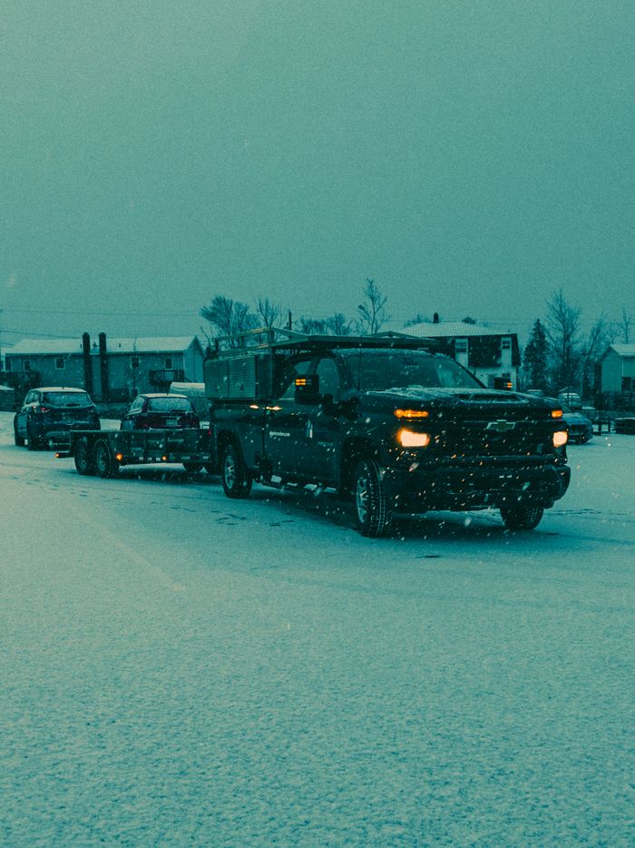 Trucks and cars drive through a snow-covered road in a serene winter landscape.