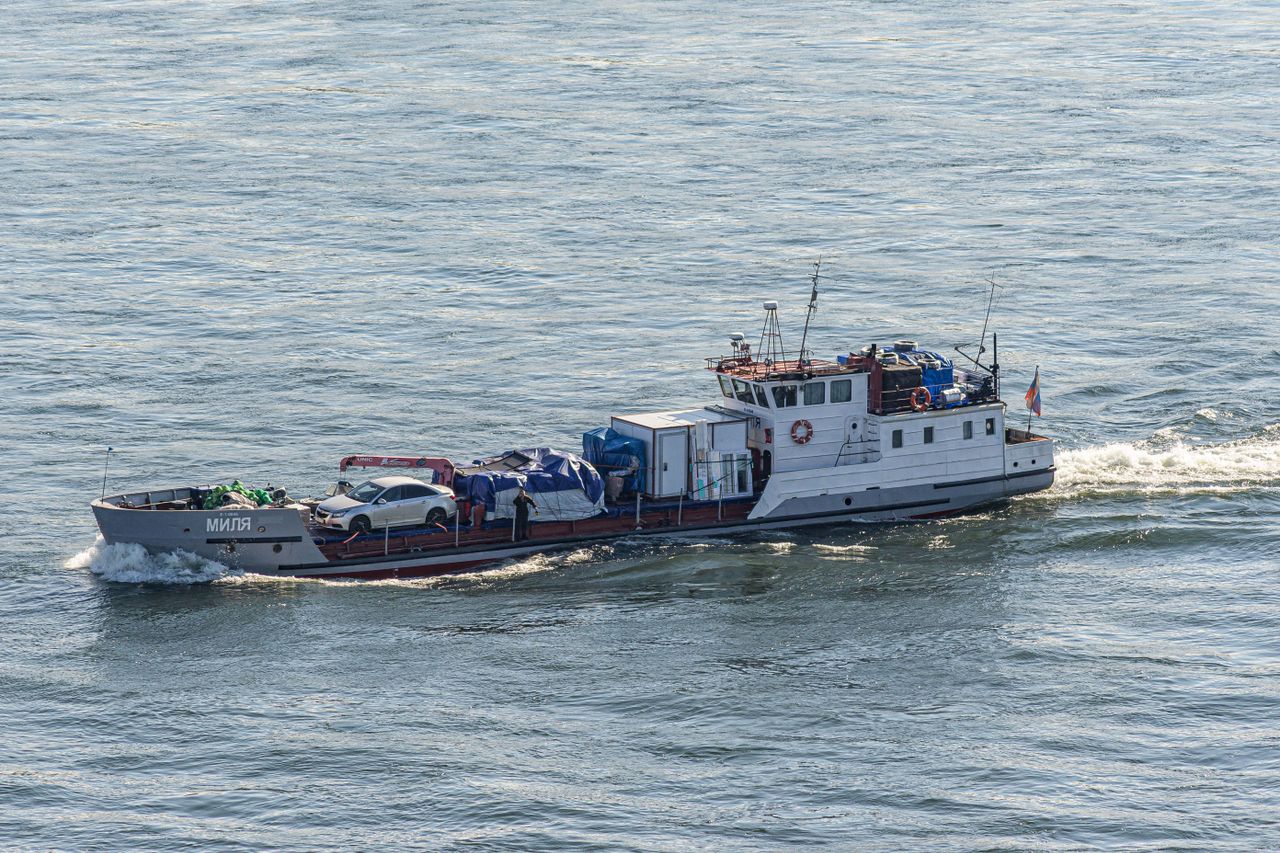 A cargo boat on a river carrying vehicles and goods, showcasing transportation and logistics in a natural setting.