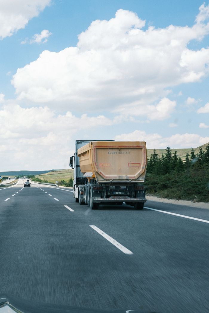 A cargo truck travels on a highway beneath a bright blue sky with fluffy clouds.